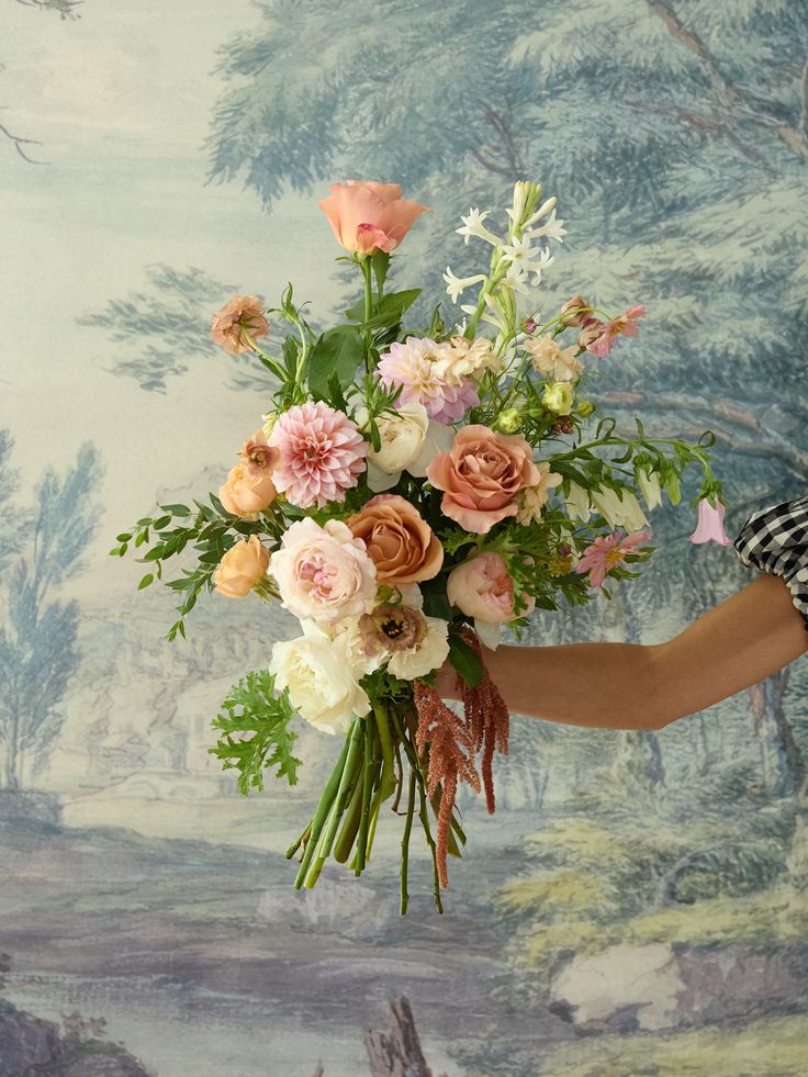 a woman holding a bouquet of flowers in front of a wall with a painting on it