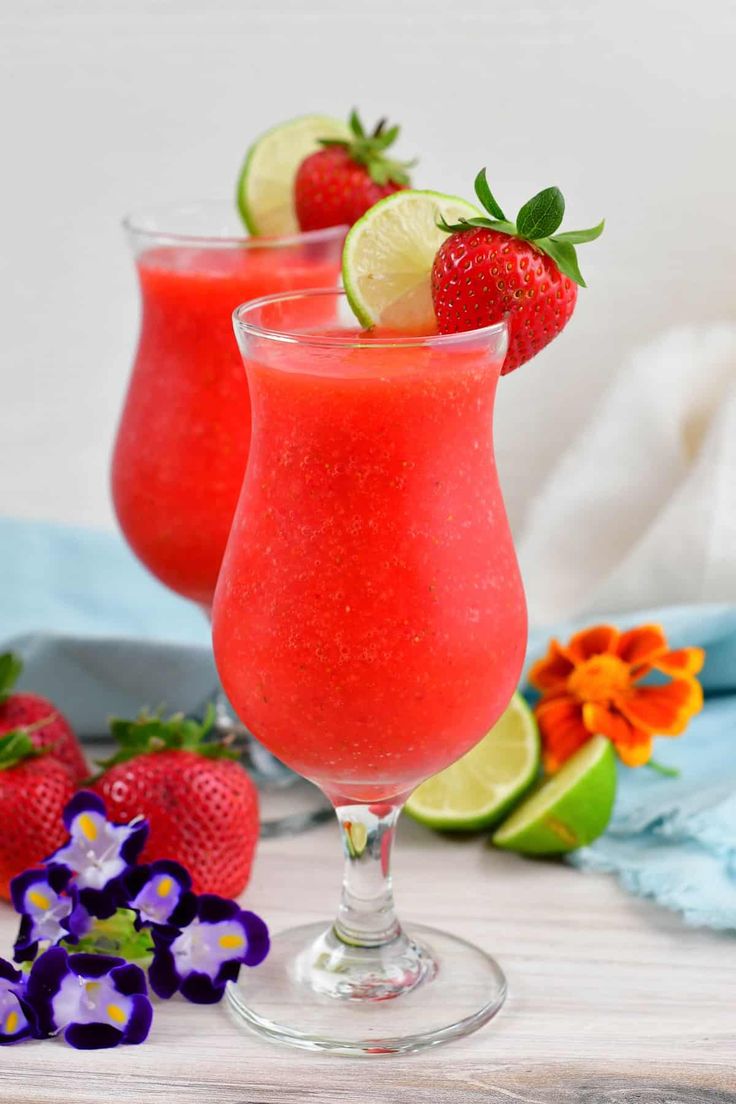 two glasses filled with strawberry margaritas and garnished with lime, strawberries