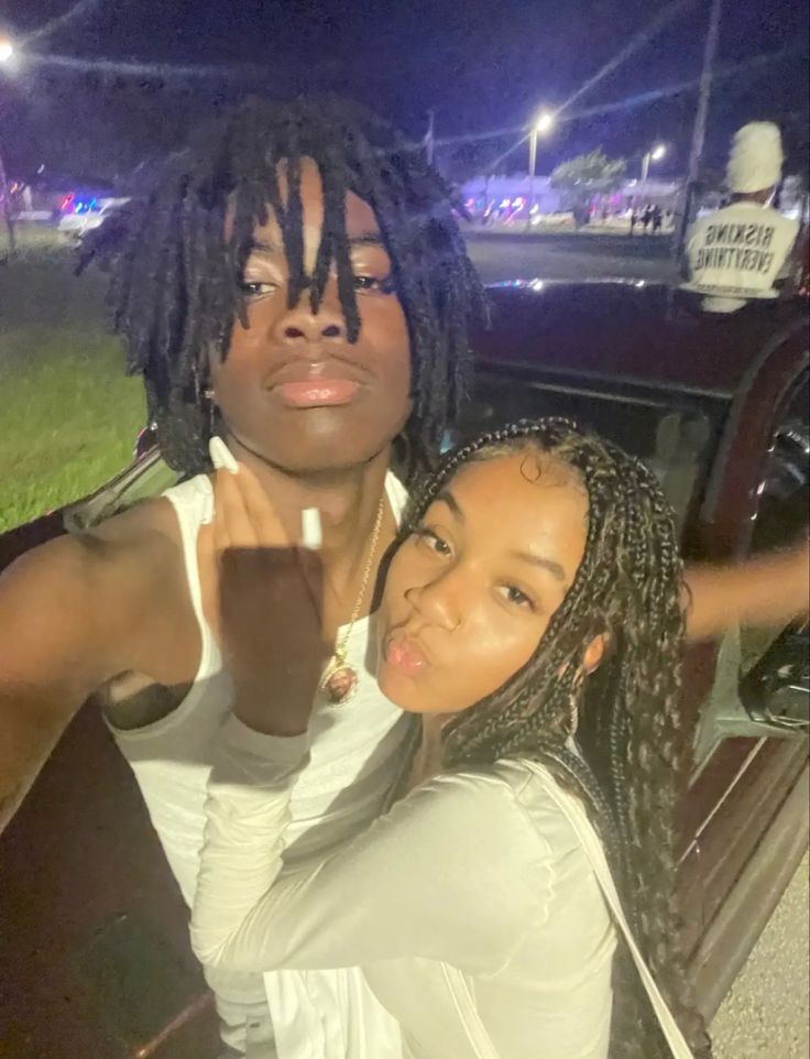 two young women posing for a photo in front of a car with their arms around each other