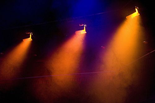 three spotlights are shining brightly on a stage with blue and yellow lights in the background