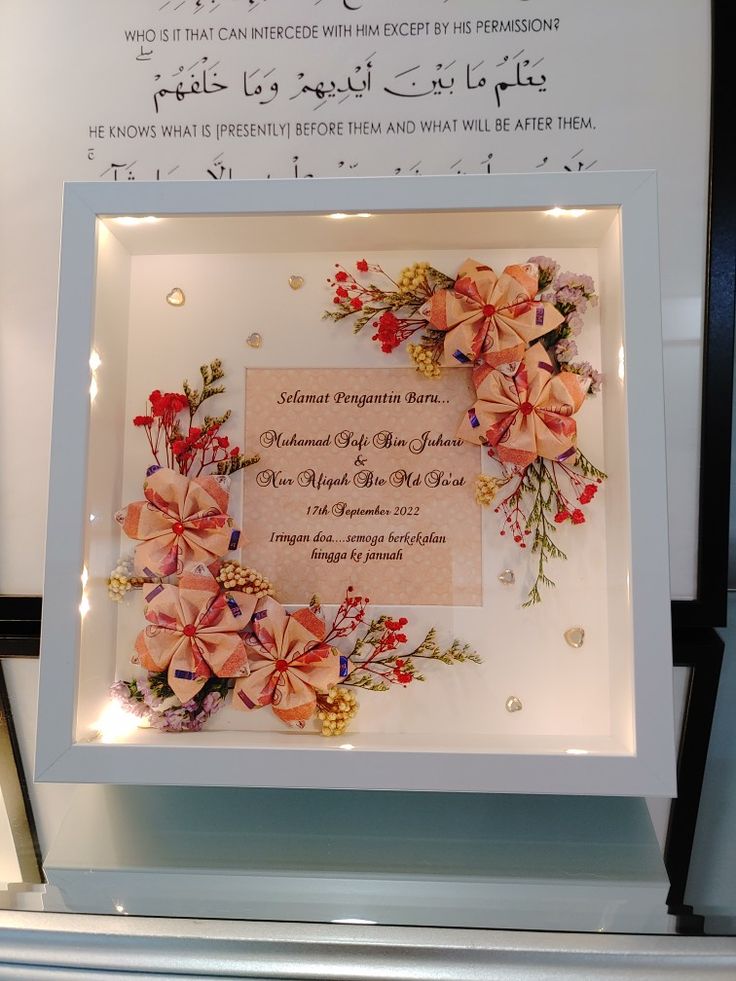 a framed wedding card with flowers and ribbons on it's display case in front of a sign that reads,