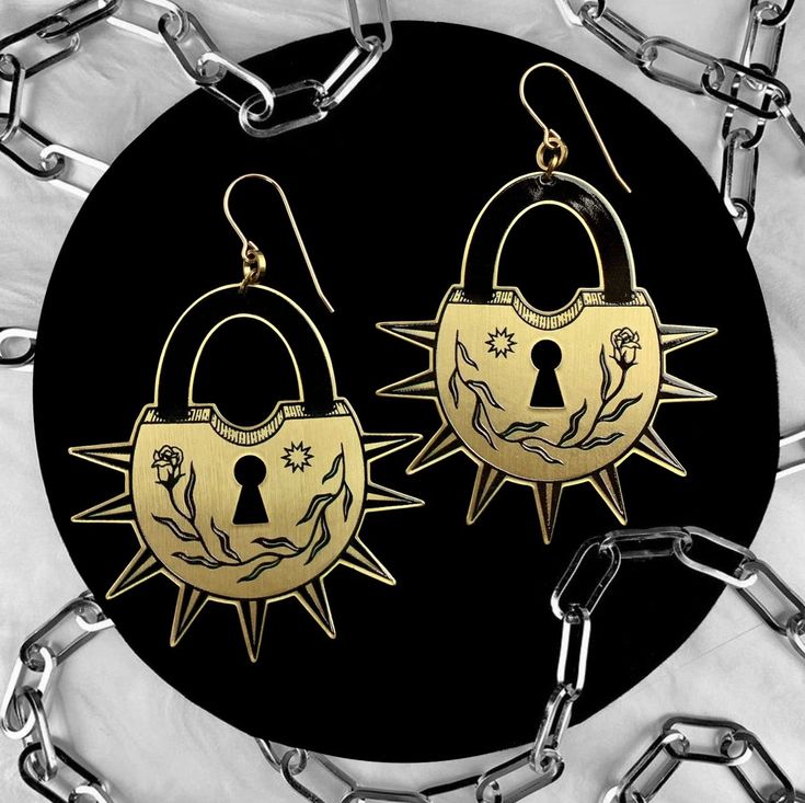 pair of golden earrings with lock and key on black circular plated surface surrounded by chain link