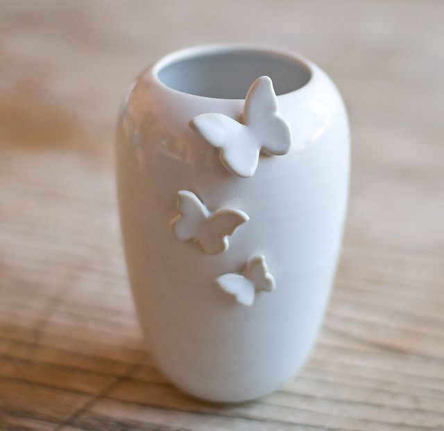 a white vase sitting on top of a wooden table with butterflies painted on the side