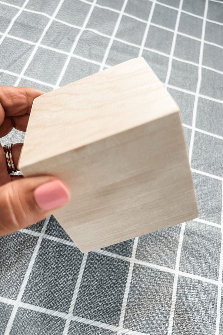 a person holding a small wooden object in their left hand on a gray and white checkered surface