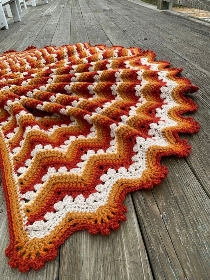 an orange and white crocheted afghan on a wooden deck