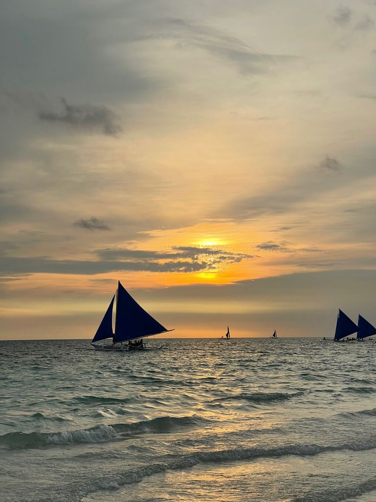 three sailboats are sailing in the ocean at sunset