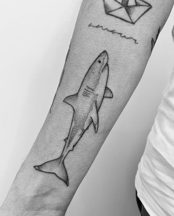 a man's arm with a shark and an origami paper boat on it