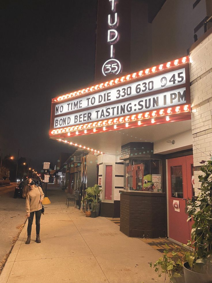 a person standing on the sidewalk in front of a building with a sign that says, no time to die 3500 455 bond beer tasting sun ipm