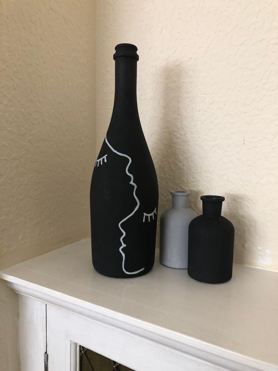 a black vase sitting on top of a white mantle next to two small bottles with faces drawn on them