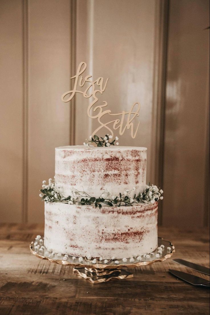 a wedding cake is decorated with white frosting and greenery as the topper