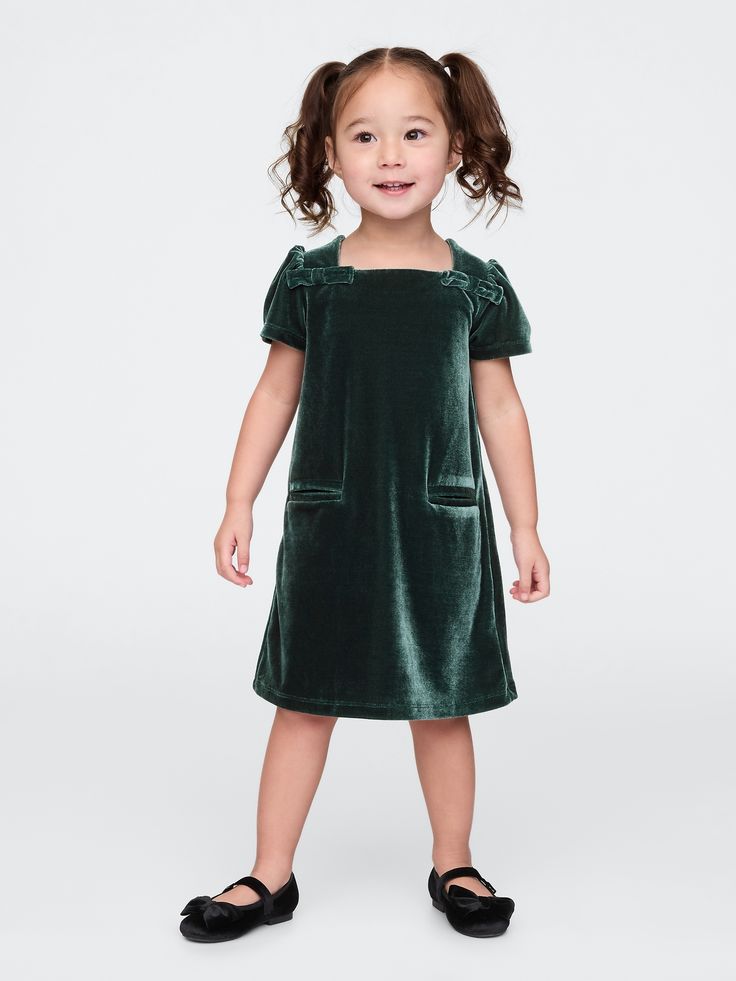 Soft, stretch velour dress.  Square neck with back button closures.  Short puff sleeves.  Bow details at front.  Front welt pockets.  This dress is made with 95% recycled polyester.  Compared to virgin materials, using recycled materials helps to reduce resource use and waste.  Shift silhouette with an easy fit.  Hits at the knee.  Sizes range from baby to toddler. Kids Holiday Dress, Christmas Card Outfits, Dress With Shoes, Essex Green, Toddler Holiday Dress, Black Toddler, Trendy Christmas Outfits, Santa Photos, Toddler Dresses