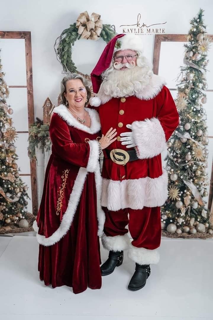 two people dressed as santa and mrs claus posing for a photo in front of christmas decorations