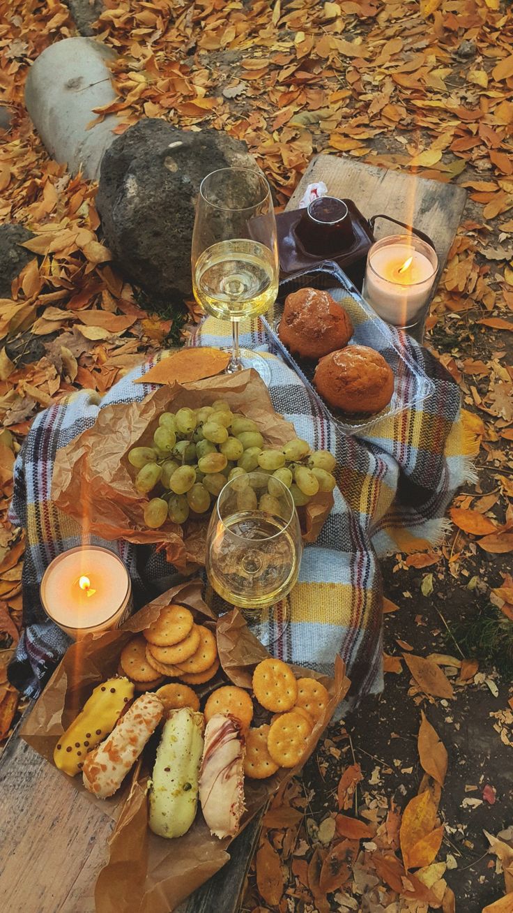 a table topped with food and drinks on top of a leaf covered ground next to a candle