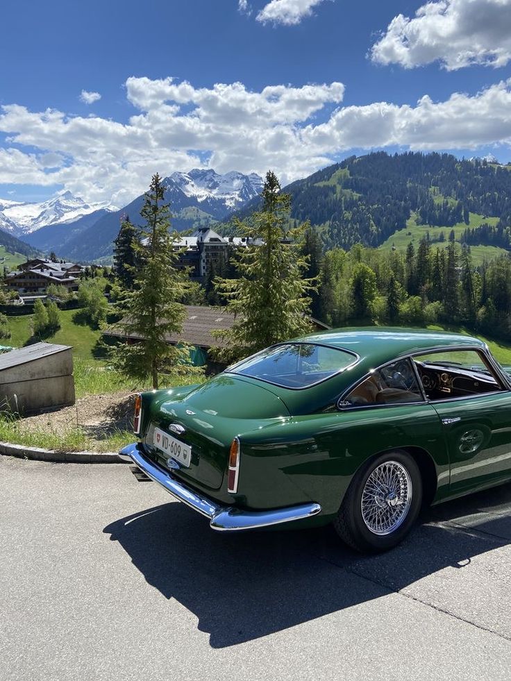 an old green car parked on the side of a road in front of some mountains