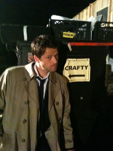 a man in a trench coat and tie standing next to a black box with graffiti on it