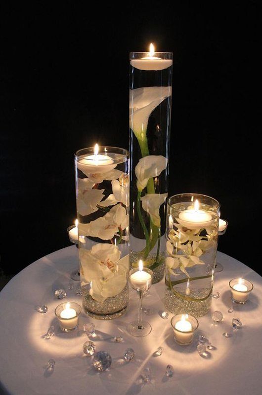 two vases filled with flowers and candles on top of a white cloth covered table