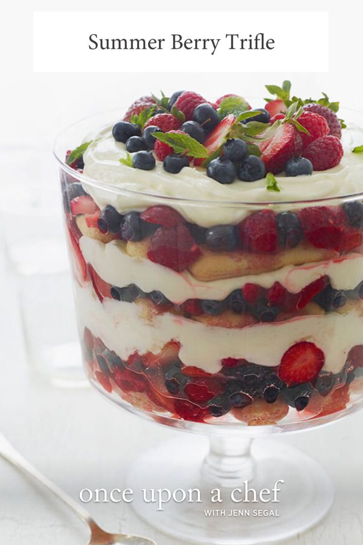 a layered berry trifle in a glass dish on a white table with text overlay that reads, summer berry trifle