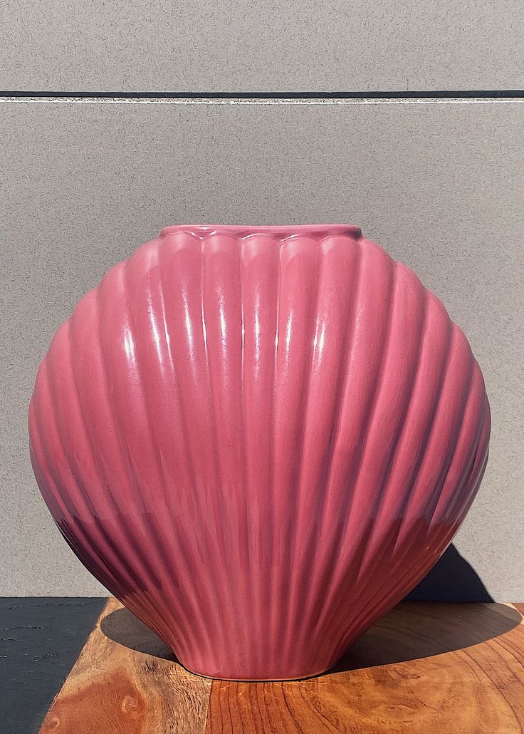 a large pink vase sitting on top of a wooden table next to a gray wall