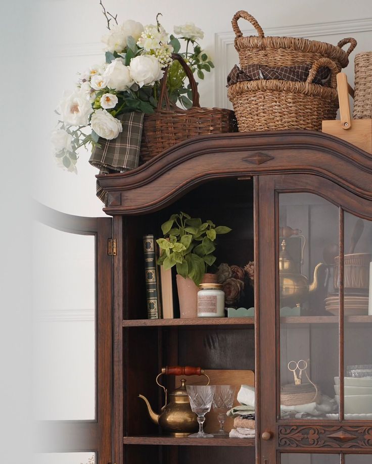 an old china cabinet with flowers and other items on the top shelf in front of it