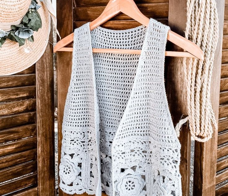 a white crocheted top hanging on a wooden wall next to a straw hat