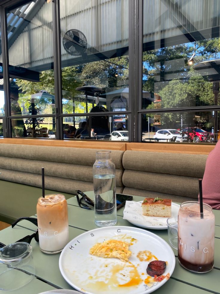 a table with two plates of food and drinks on it in front of a window