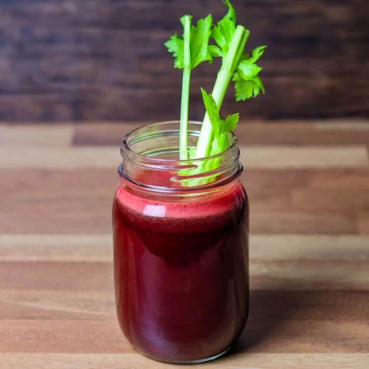 a jar filled with red liquid sitting on top of a wooden table next to a green leafy plant