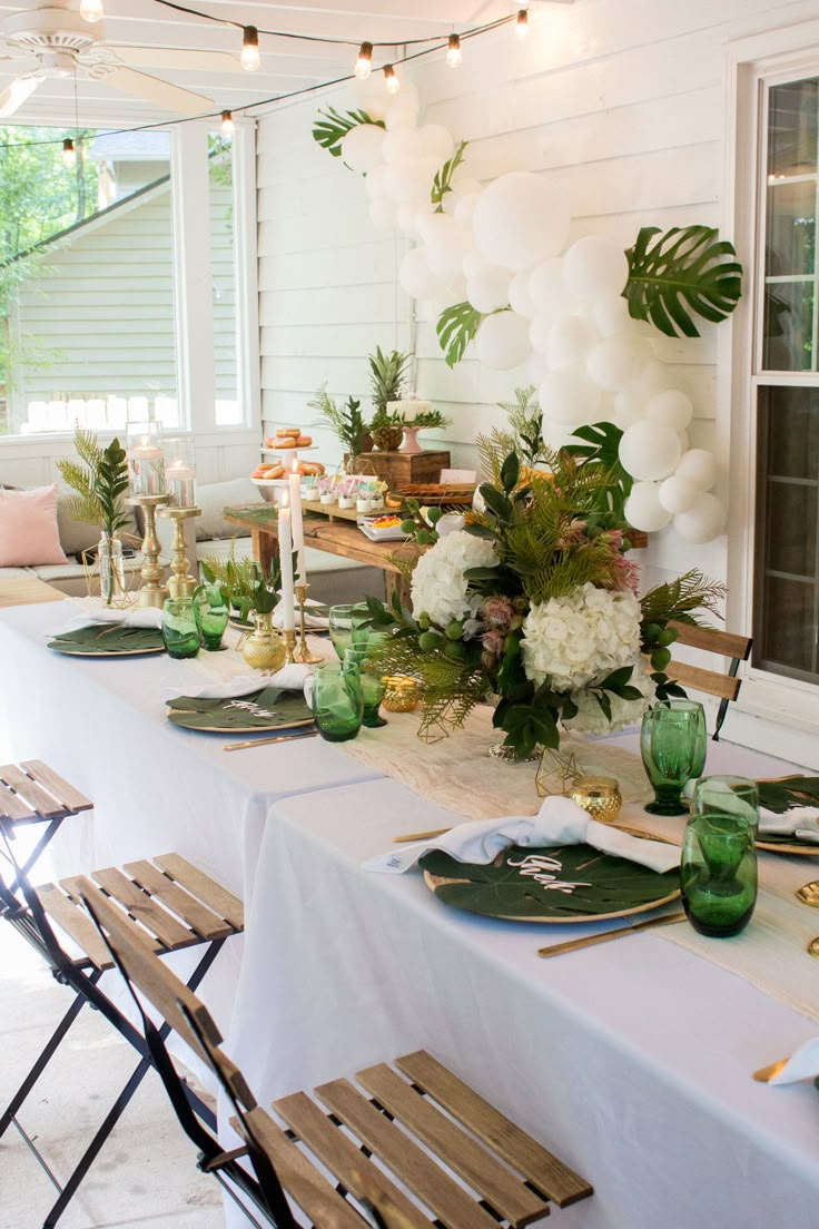 a long table with white flowers and greenery is set up for an outdoor party