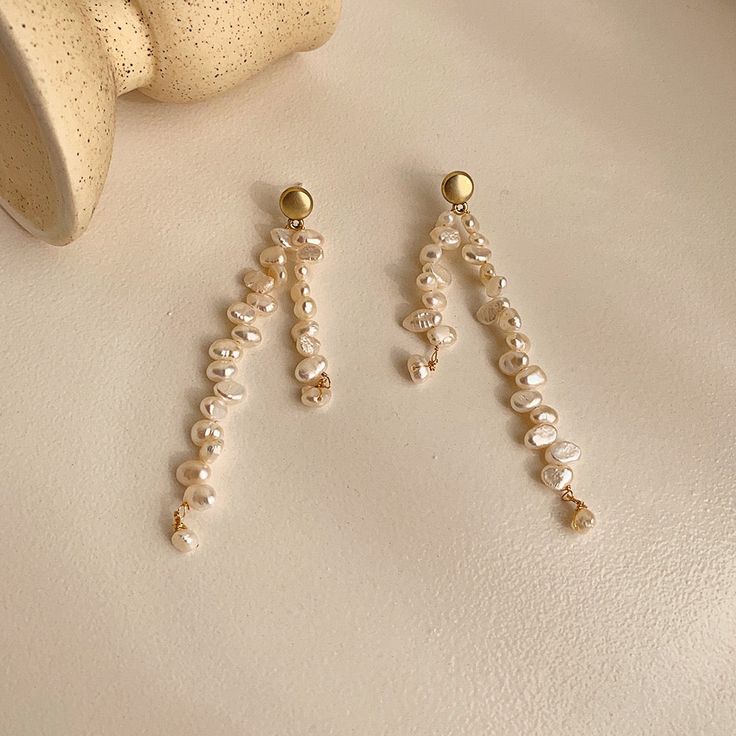 Introducing our exquisite Pearl Drop Earrings, a true masterpiece in asymmetrical elegance. These earrings are meticulously handcrafted using a combination of real freshwater pearls and 18 karat yellow gold vermeil. The unique wavy design, with its beige pearls and subtle, blurry details, evokes a sense of graceful fluidity. Embrace the artistry of asymmetry and add a touch of ethereal beauty to your style with these light white wonders. Elegant Handmade Gold Plated Pearl Earrings, Handmade Elegant Gold Plated Pearl Earrings, Gold Long Drop Pearl Pendant Earrings, Gold Long Drop Earrings With Pearl Pendant, Graceful Pearl Dangle Earrings, Single Dangle Pearl Earring, Single Long Drop Pearl Earring, Single Drop Pearl Earring, Yellow Gold Long Drop Pearl Earrings