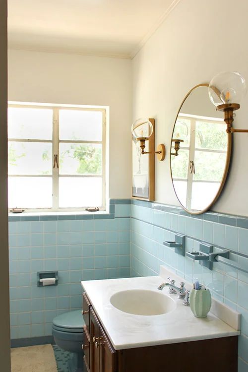 a bathroom with blue tiles and a white sink under a round mirror on the wall