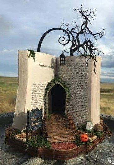 an open book sculpture sitting on top of a rock covered in grass and vines with a tree growing out of it