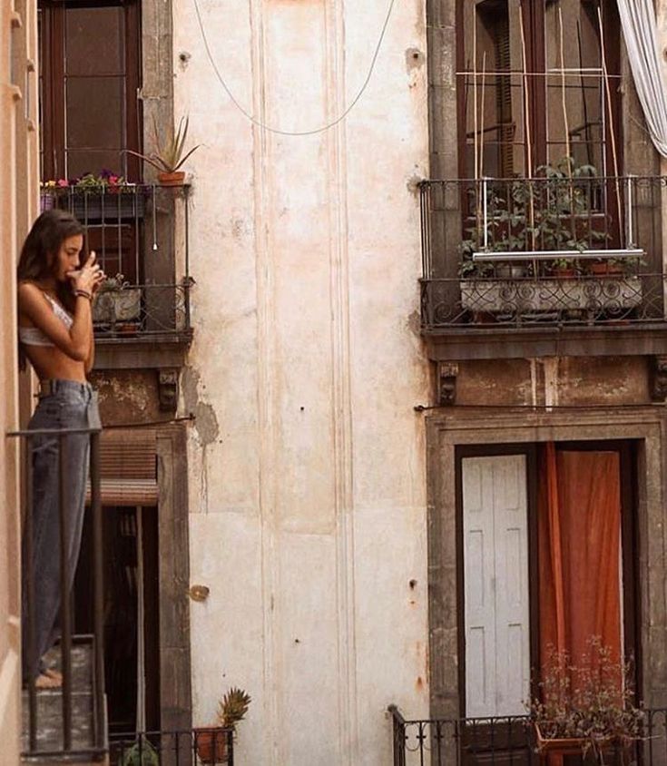 a woman is standing on the balcony talking on her cell phone while looking out at the street