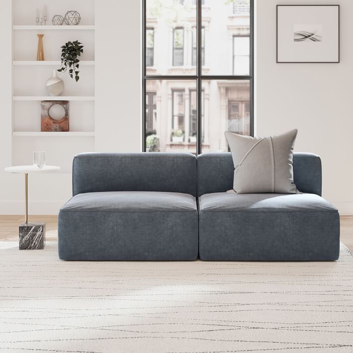 a gray couch sitting in front of a window next to a white wall and floor