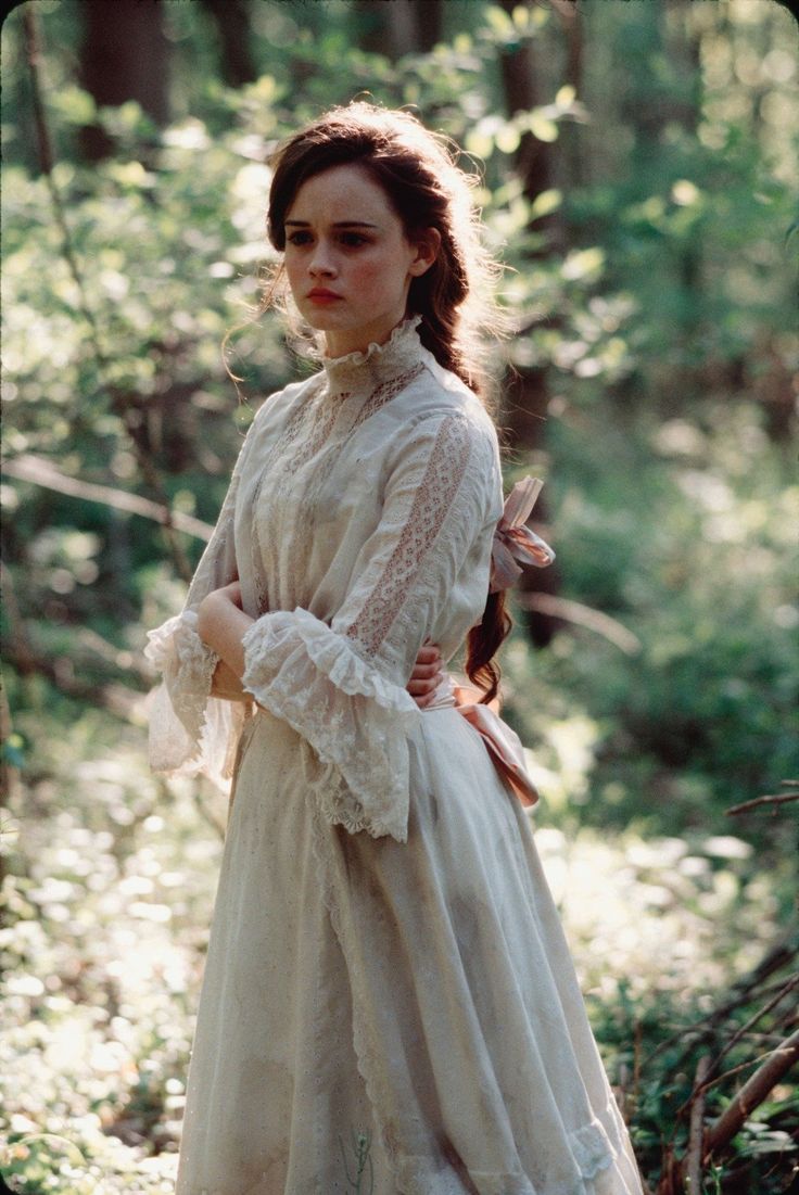 a woman standing in the woods wearing a white dress and holding her hands on her hips