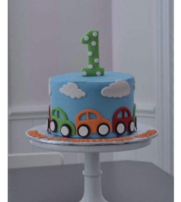 a blue cake with cars on it sitting on top of a white pedestal in front of a window