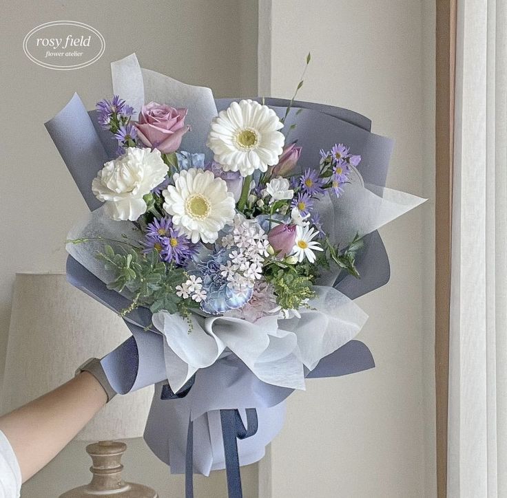 a bouquet of flowers is being held by a woman's hand near a vase