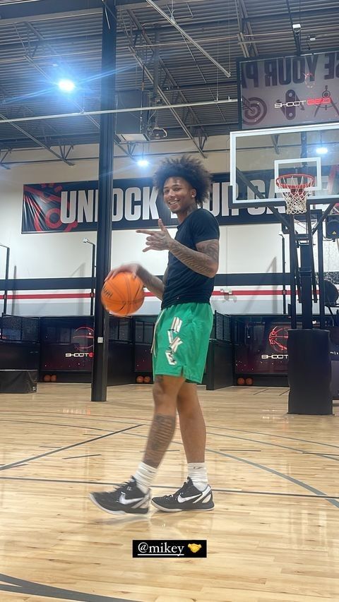 a young man holding a basketball on top of a hard wood floor in a gym