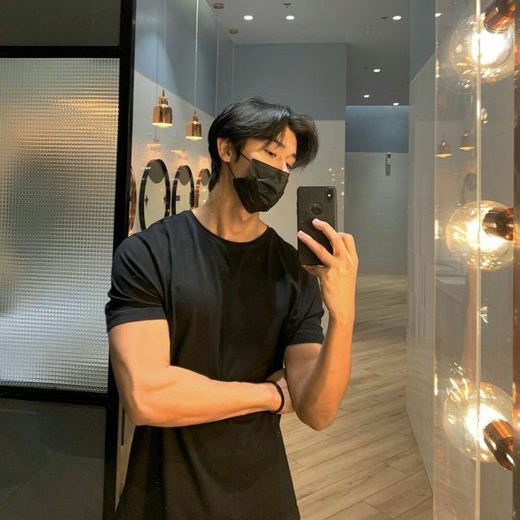 a man wearing a face mask taking a selfie in front of a mirror with his cell phone