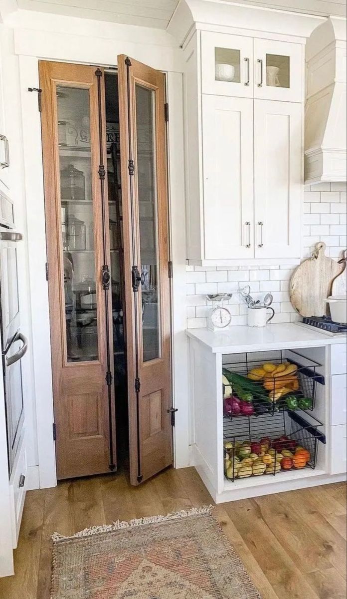 a kitchen with white walls and wooden floors has two doors open to reveal the pantry