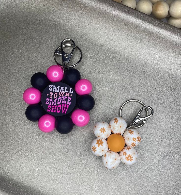 a small flower keychain sitting on top of a metal sink next to a pink and black key chain