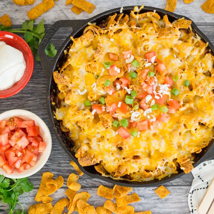 a casserole dish with tortilla chips, sour cream and salsa on the side