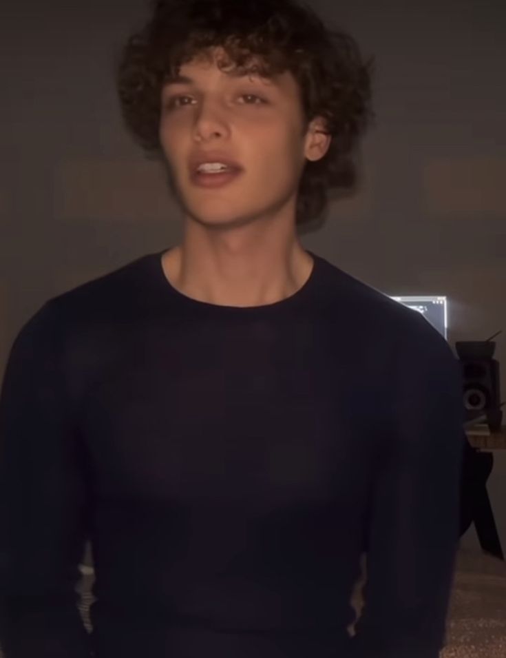 a young man with curly hair wearing a black shirt and standing in front of a camera