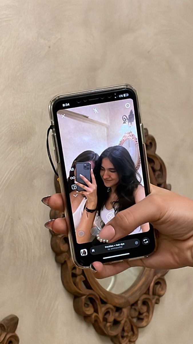 a woman taking a selfie with her cell phone in front of a mirror that is hanging on the wall