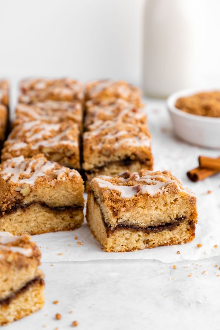 cinnamon roll bars with icing sitting on top of a table next to some cinnamon sticks