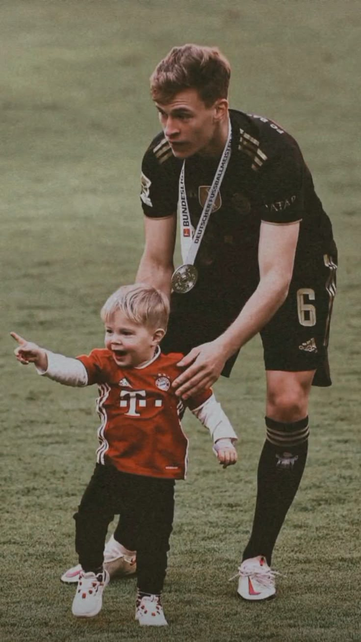 a young man holding onto a small child on top of a grass covered soccer field