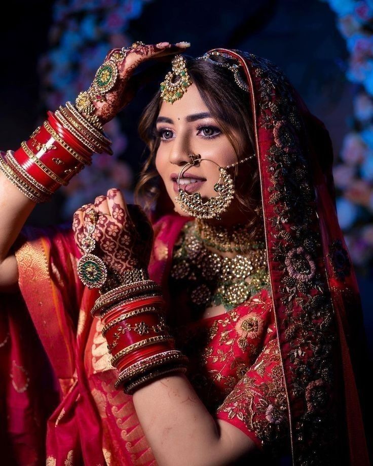 a woman in a red and gold bridal outfit holding her hands up to her head