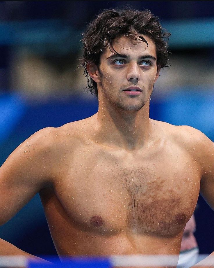 a shirtless male tennis player holding his racket in one hand and looking off to the side