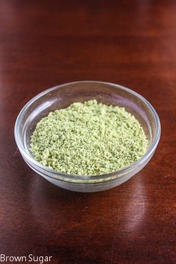 a bowl filled with green powder sitting on top of a wooden table next to a glass container