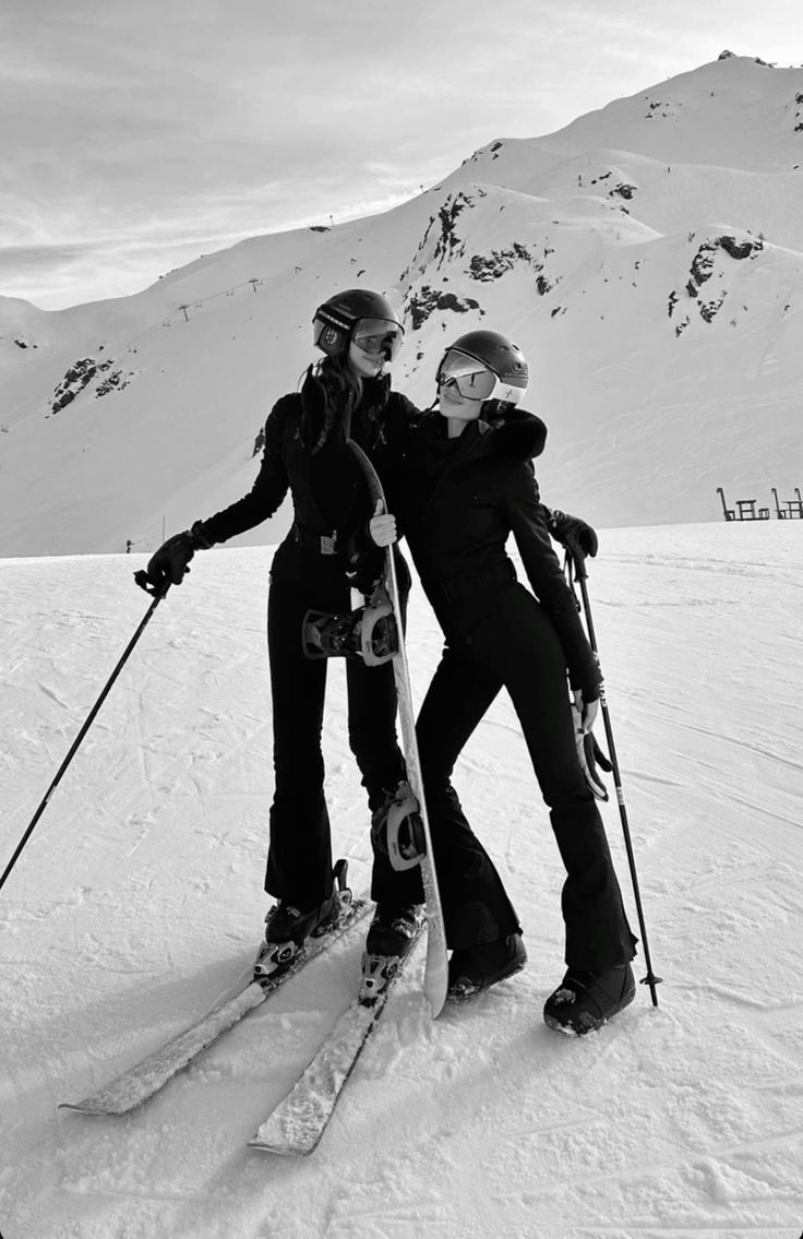 two people on skis standing in the snow with their arms around each other,