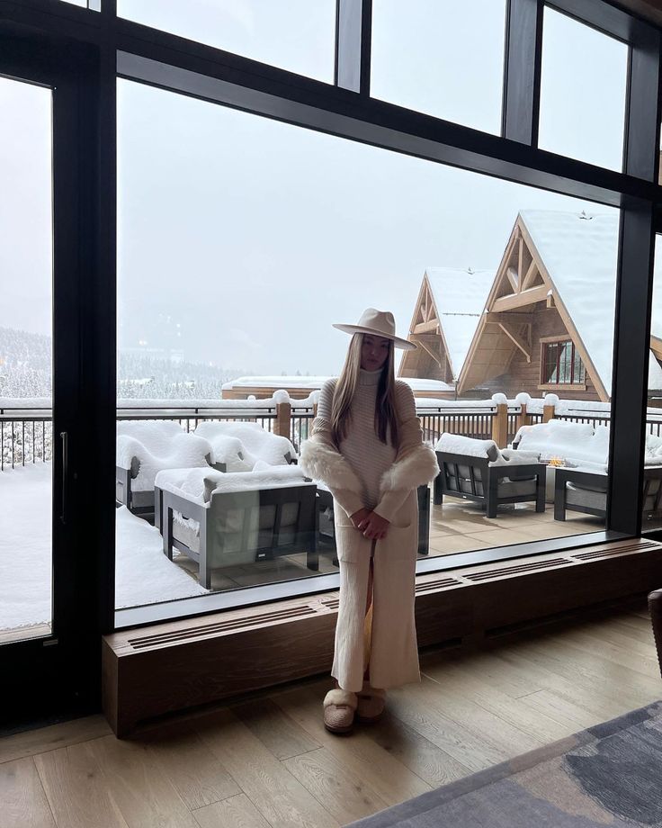 a woman standing in front of a large window with snow on the ground behind her