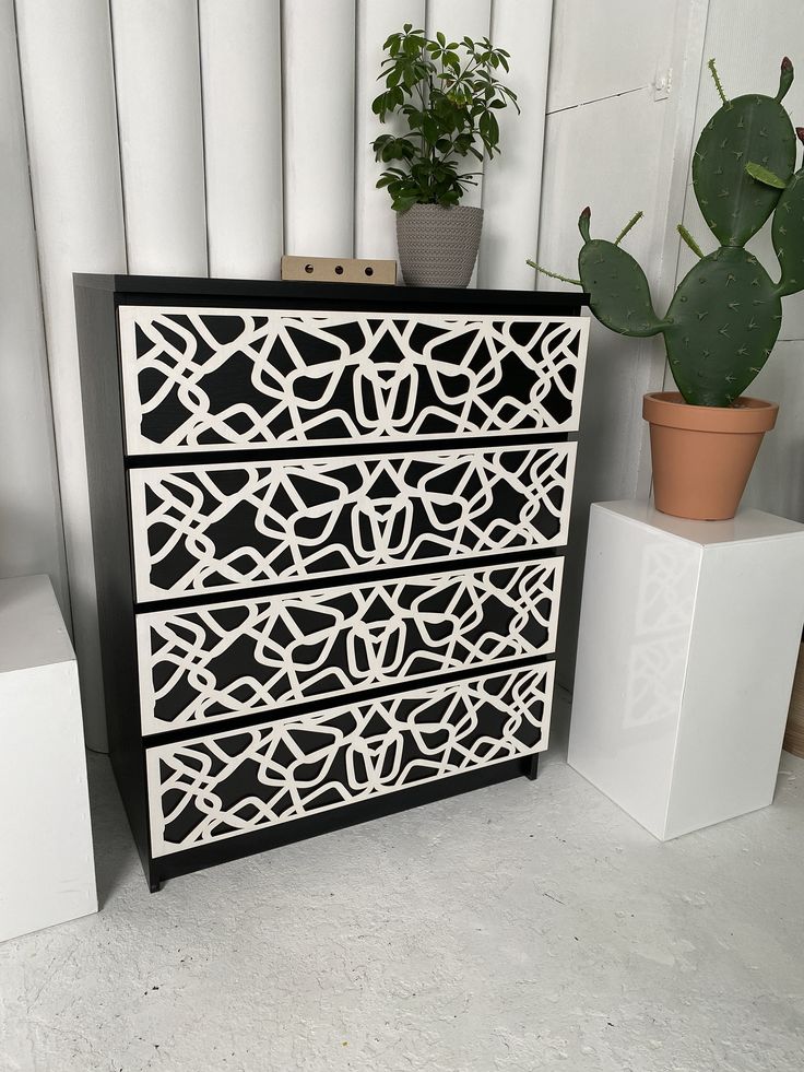 a black and white chest of drawers next to a potted cacti plant